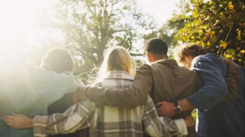 photo of the backs of men and women in a line with their arms around each other while outside on a fall day