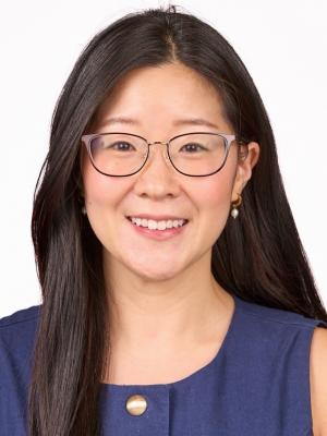 East asian american woman wearing glasses, smiling, with long black hair and a navy top with a gold button