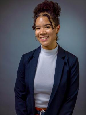 Professional headshot of Tara wearing a black blazer and white shirt, against a gray background.