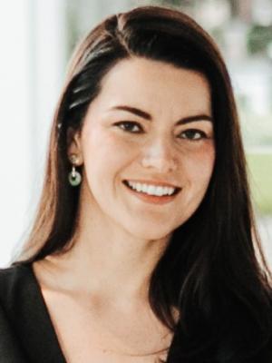 Professional headshot of Dr. Cristina Risco, facing the camera and smiling, with long dark hair, wearing a black top and earrings against a softly blurred background.
