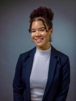 Professional headshot of Tara wearing a black blazer and white shirt, against a gray background.