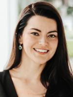 Professional headshot of Dr. Cristina Risco, facing the camera and smiling, with long dark hair, wearing a black top and earrings against a softly blurred background.
